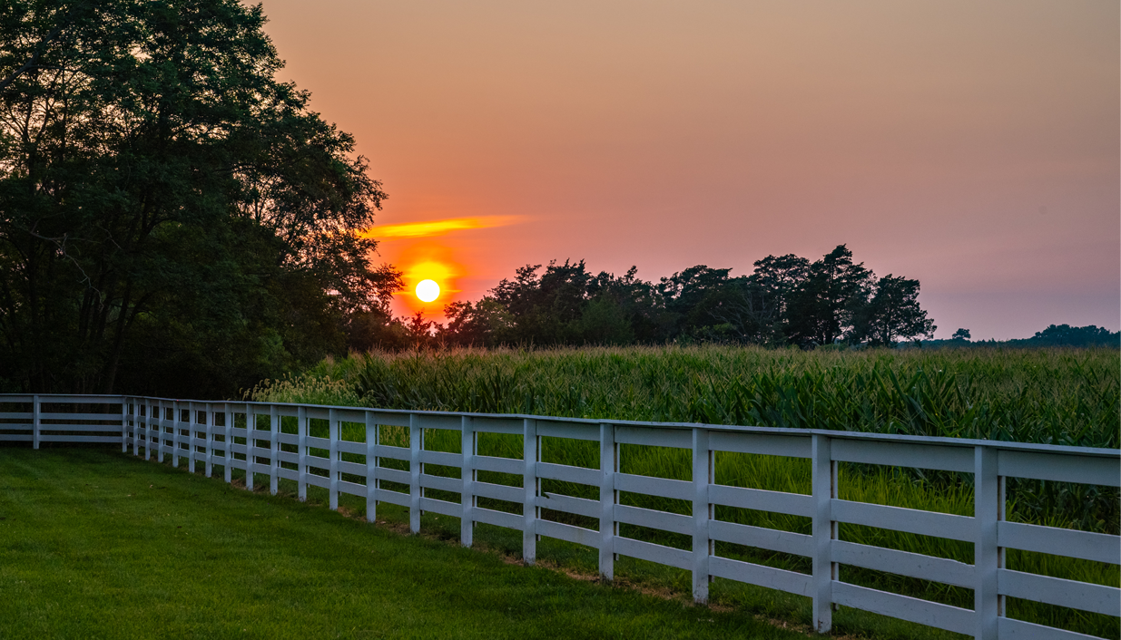 the sun setting behind a white fence