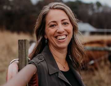 a smiling woman holding a wooden pole in a field