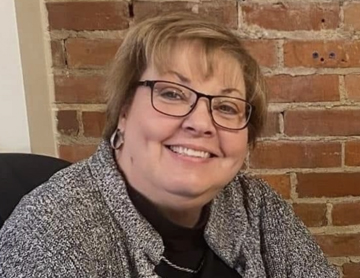a woman wearing glasses sitting in front of a brick wall