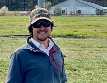 a man wearing a hat and sunglasses standing in a field