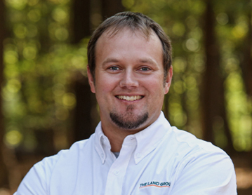 a man in a white shirt standing in front of trees