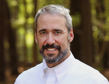 a man in a white shirt and tie standing in front of trees