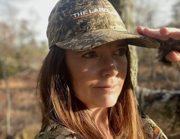 a woman in a camo jacket and hat holding a branch