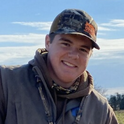 a man wearing a hat and jacket standing in a field