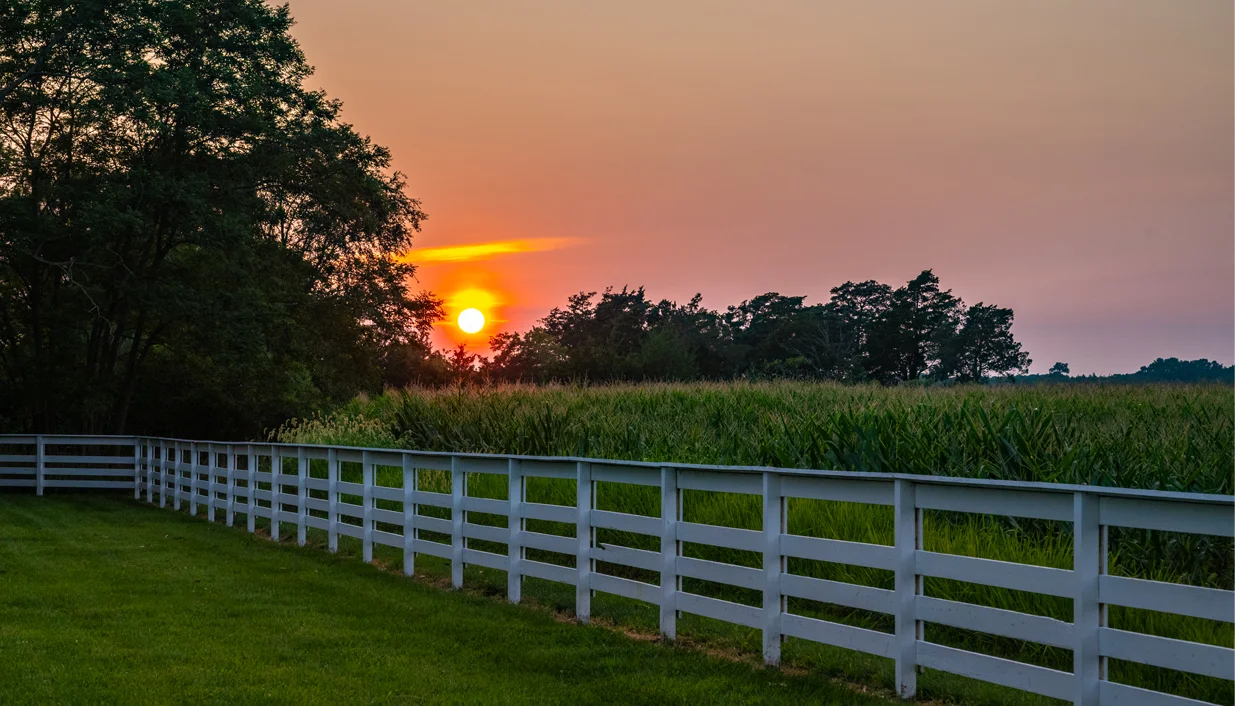 the sun setting behind a white fence
