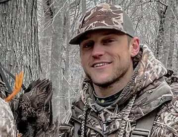 a man holding a bird in the woods