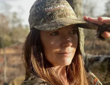 a woman in a camo jacket and hat holding a branch